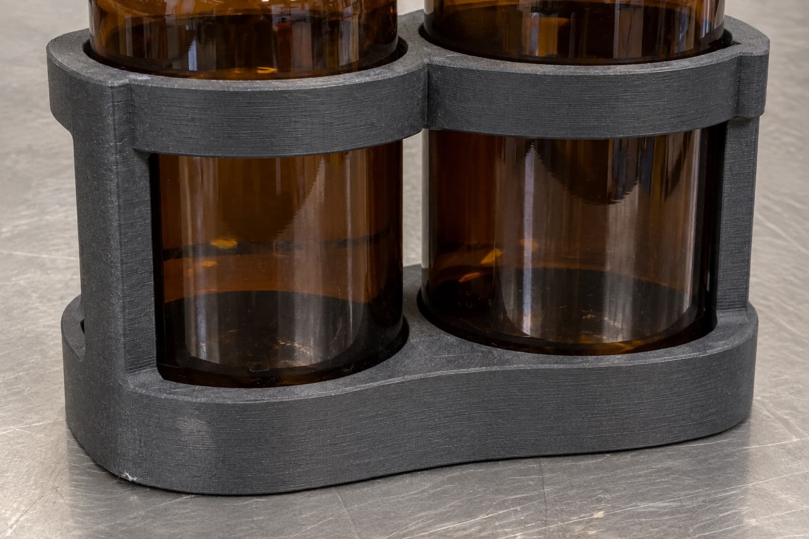 3D printed PPS-CF carrier holding two amber solvent bottles on a stainless steel bench, showing the chemical resistance PPS-CF is specified for