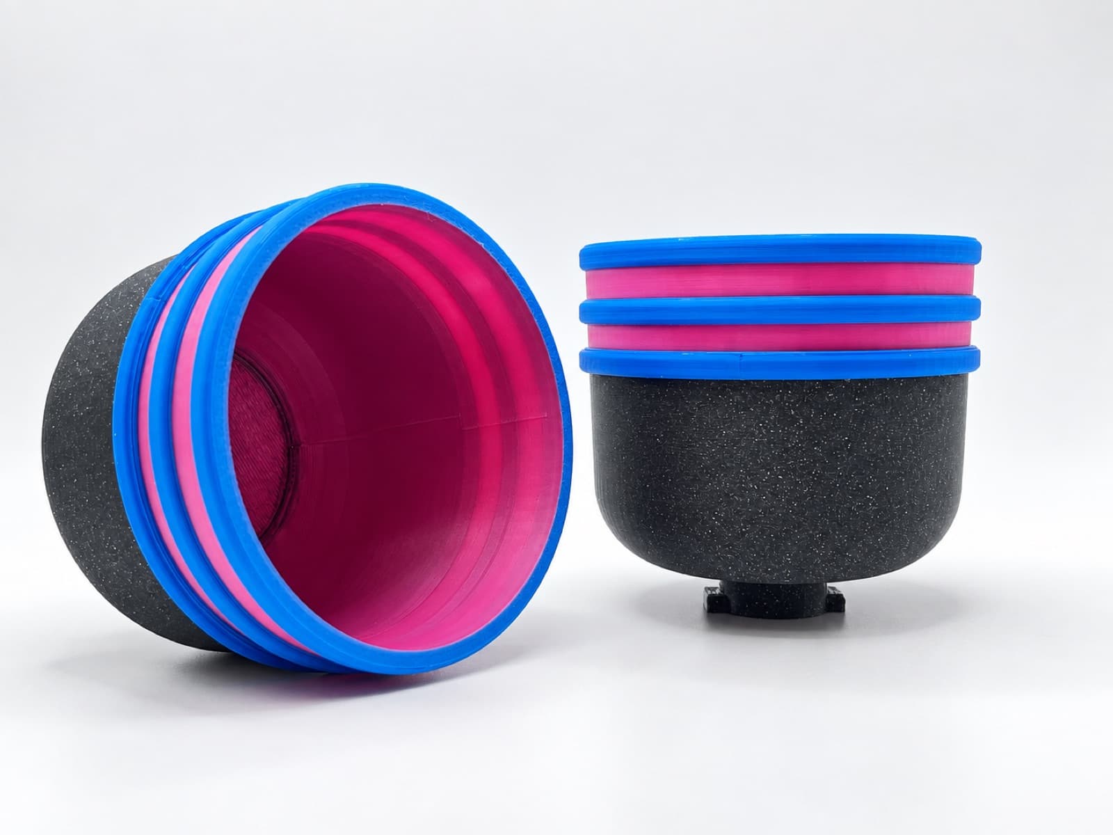 Two stacks of identical 3D printed bowl-shaped housings in blue, magenta and black on a white studio sweep