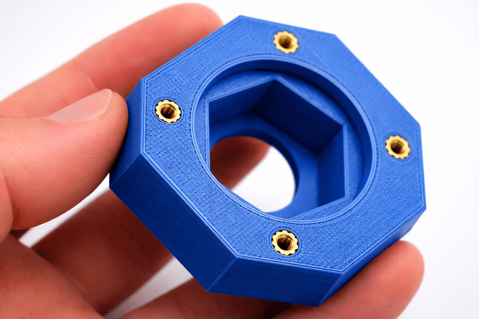 Blue octagonal 3D printed part with seven heat-set brass threaded inserts installed flush with the surface