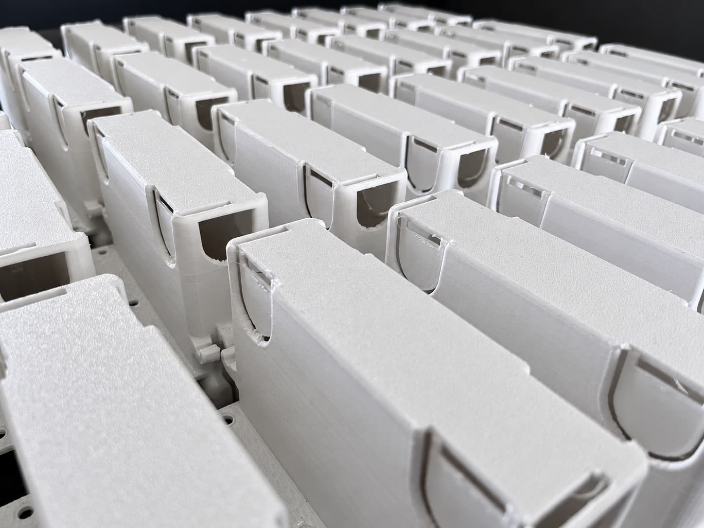 A production run of white 3D printed back boxes lined up on the bench, cable entries facing the camera