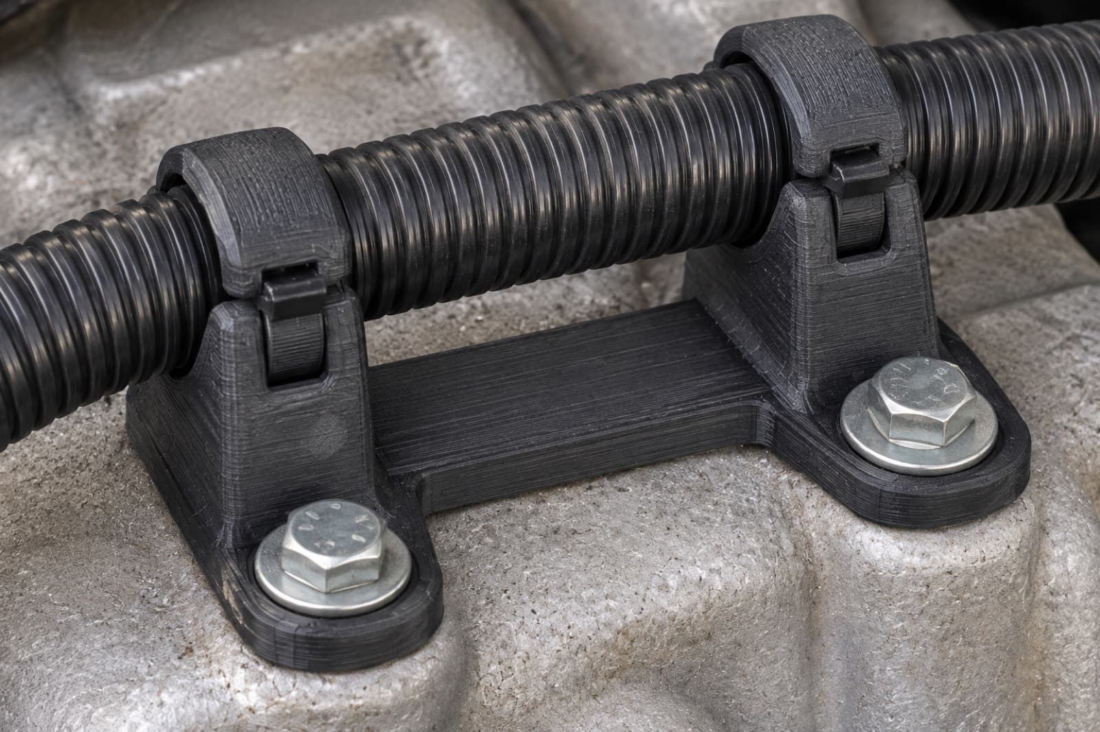 3D printed PAHT-CF conduit clamps bolted to a cast aluminium engine casting, routing corrugated conduit in a high-temperature location