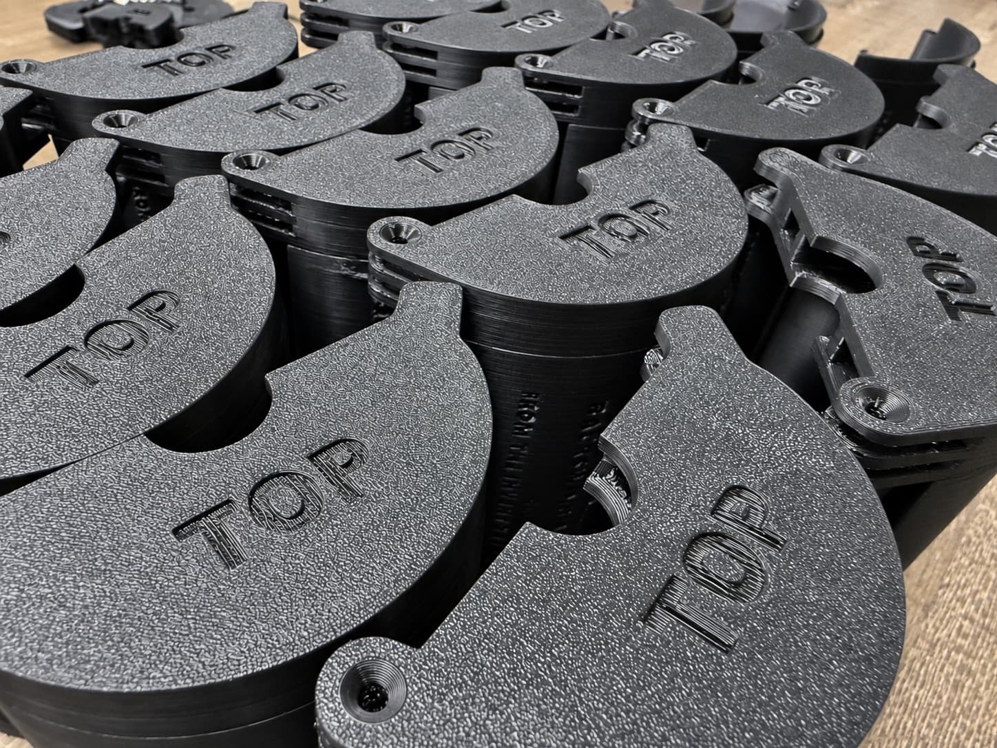 A batch of black 3D printed production caps, freshly printed and stacked on the bench before inspection