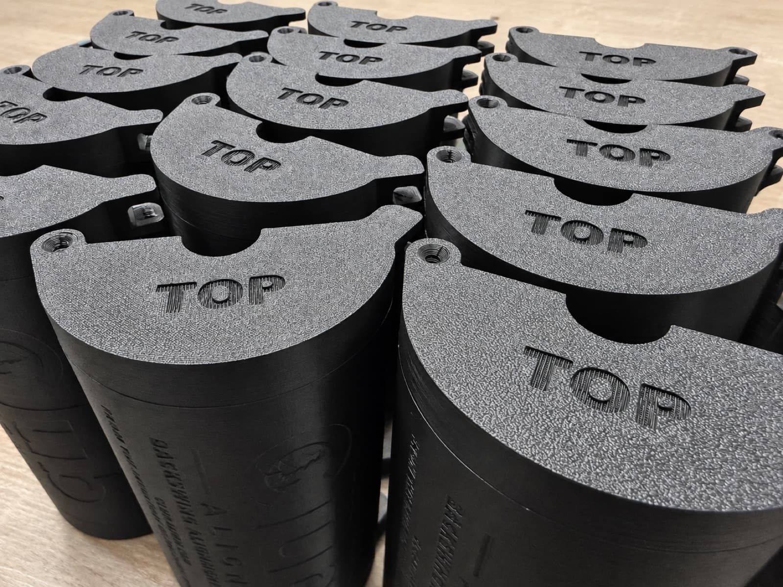 A batch of identical black 3D printed cylindrical housings on the San Diego production bench, front three-quarter view
