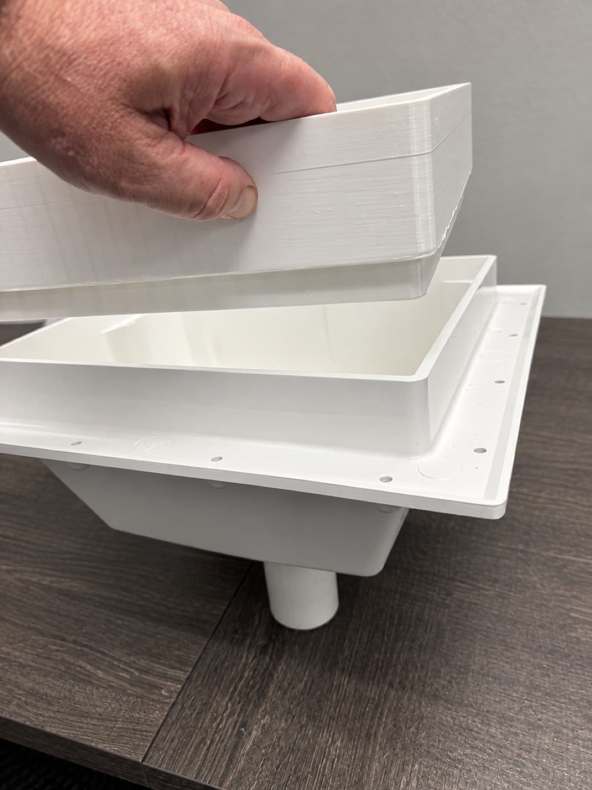 A hand lifting a 3D printed insert tray out of a large white printed recessed enclosure