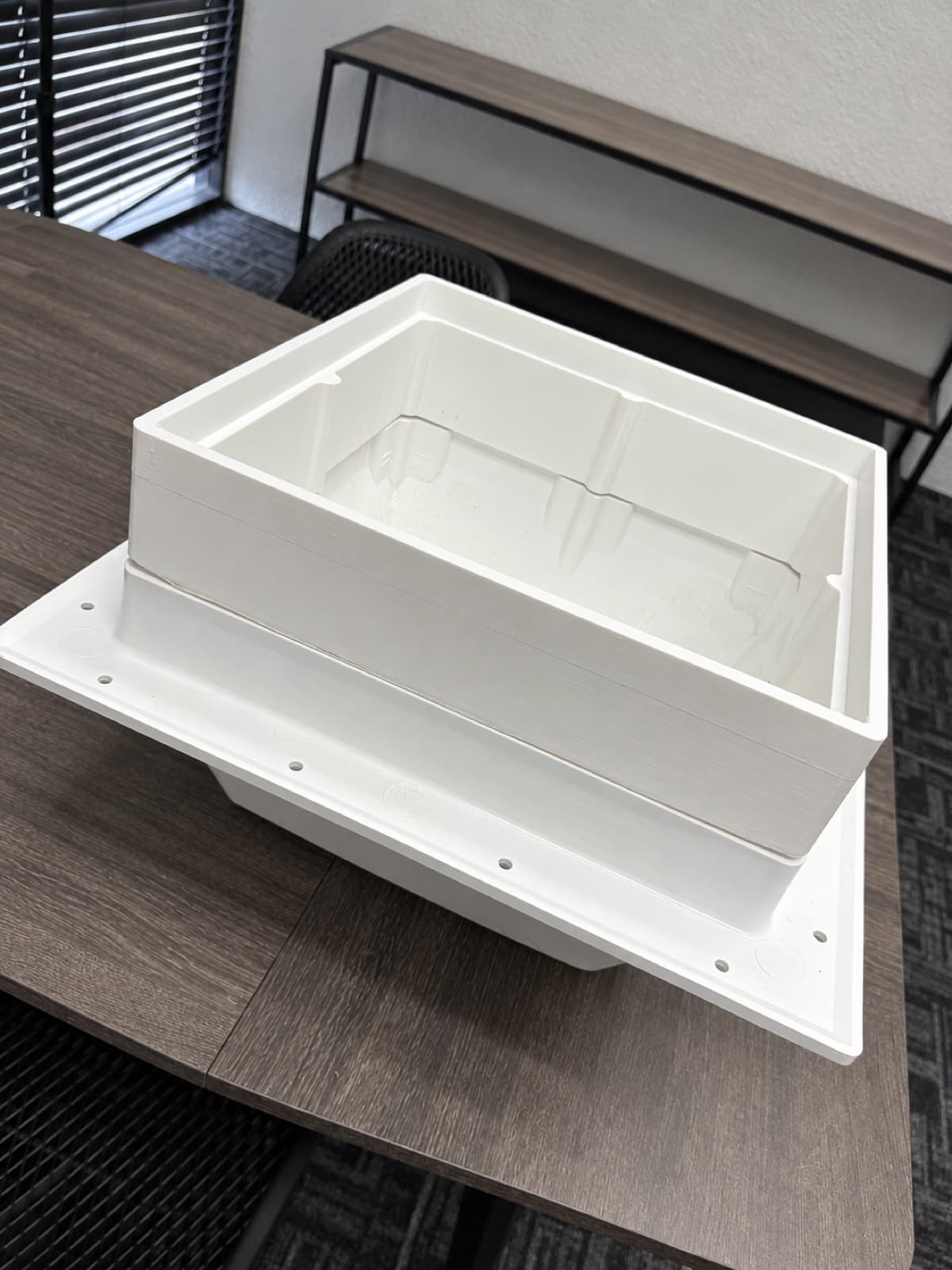 Two large white 3D printed enclosure parts, a deep insert tray and a recessed box, on a desk