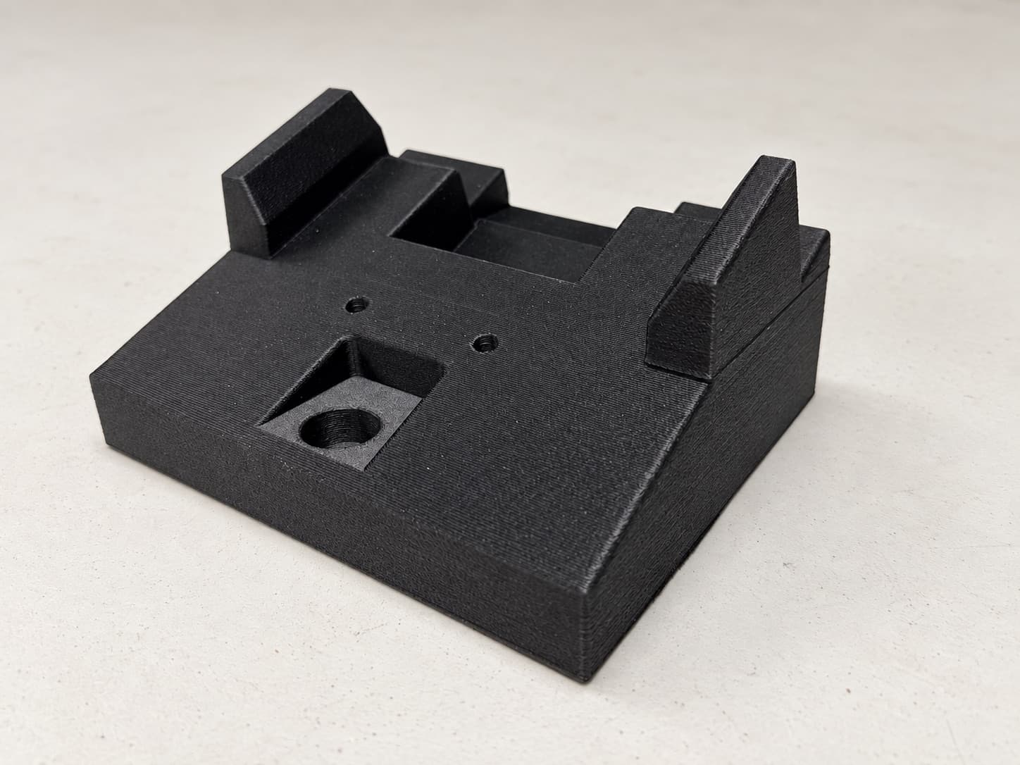 Black 3D printed locating fixture with raised stops and a threaded-insert pocket, printed as shop-floor tooling