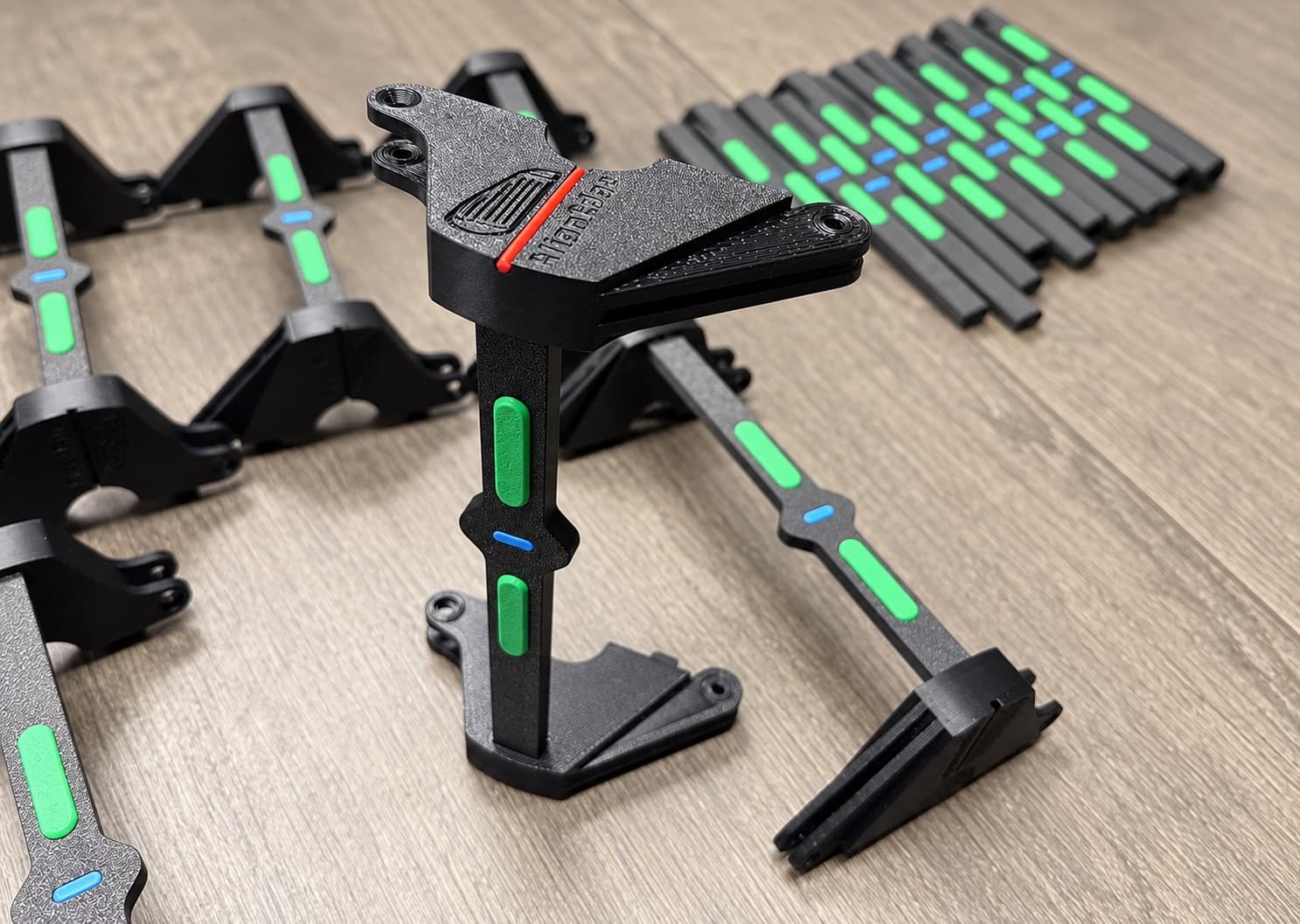 Assembled multi-part 3D printed production component with black rails and green and blue inserts, several SKUs from one batch