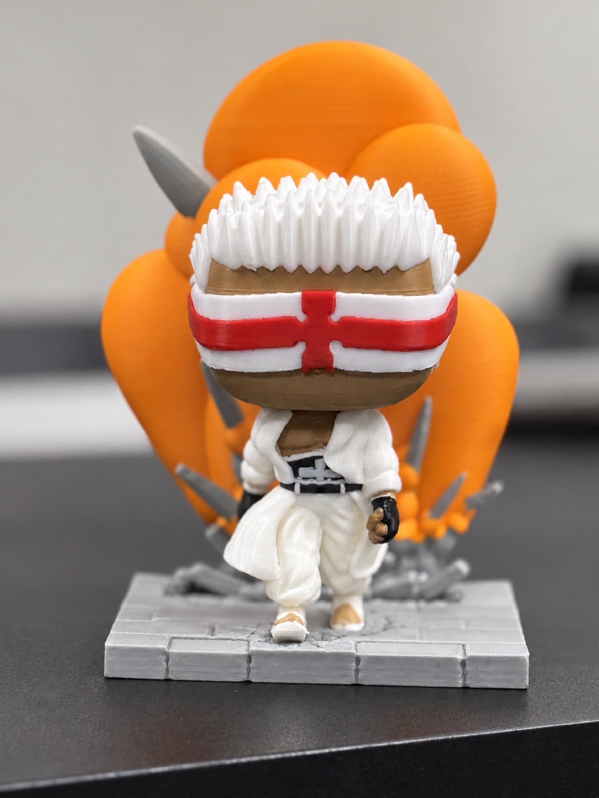 A hand-painted multi-part 3D printed collectible figure with white spiked hair and a red-and-white headband, standing on a printed stone base