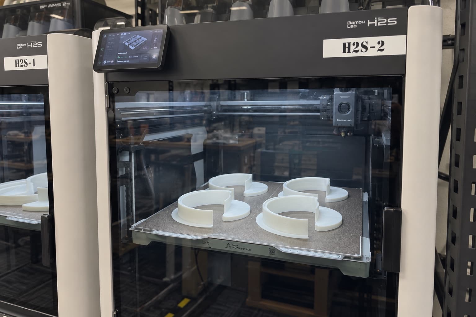 A finished batch of white 3D printed parts still on the build plate inside an open TAKT 3D production machine
