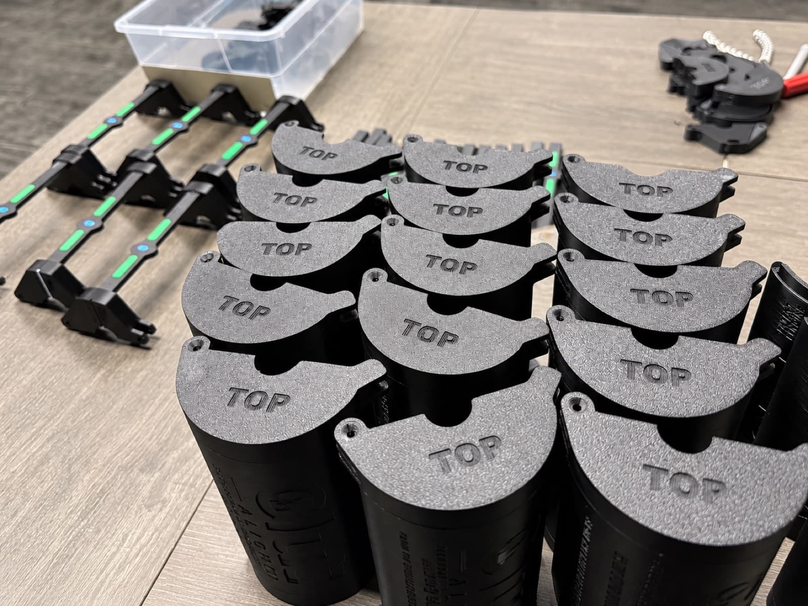 A production batch of black 3D printed housings with grey caps marked TOP, staged on the TAKT 3D bench for assembly
