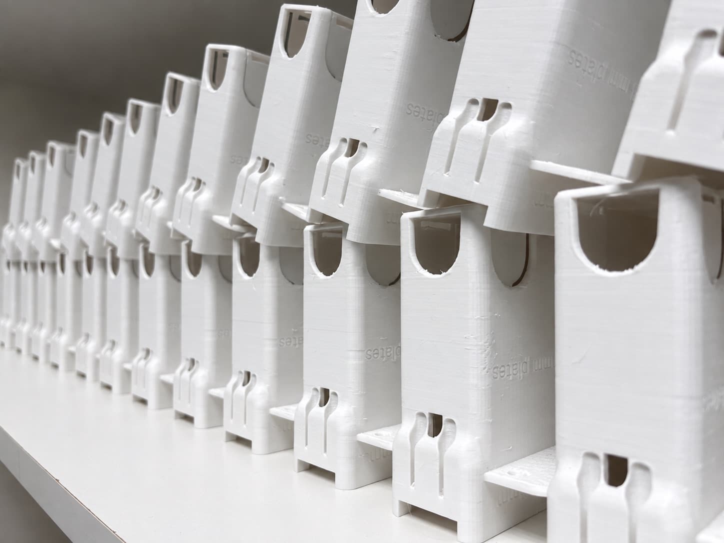 Rows of white 3D printed production housings stacked on the bench at TAKT 3D, fresh off the printers