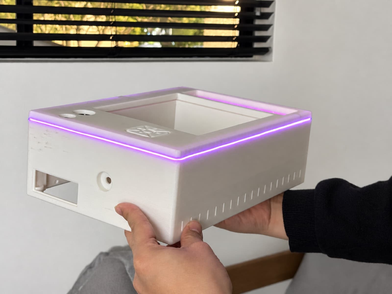 Two hands holding a finished white 3D printed electronics enclosure with an illuminated edge strip