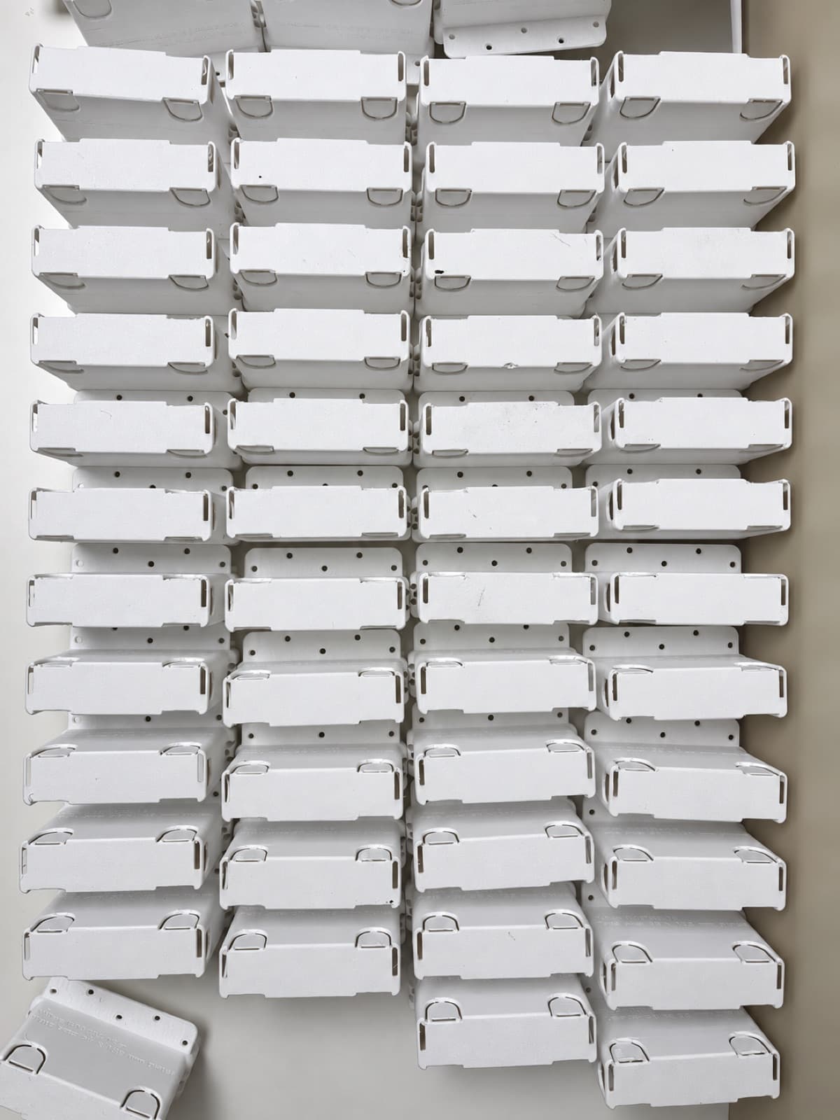 Overhead view of roughly forty identical white 3D printed housings arranged in rows