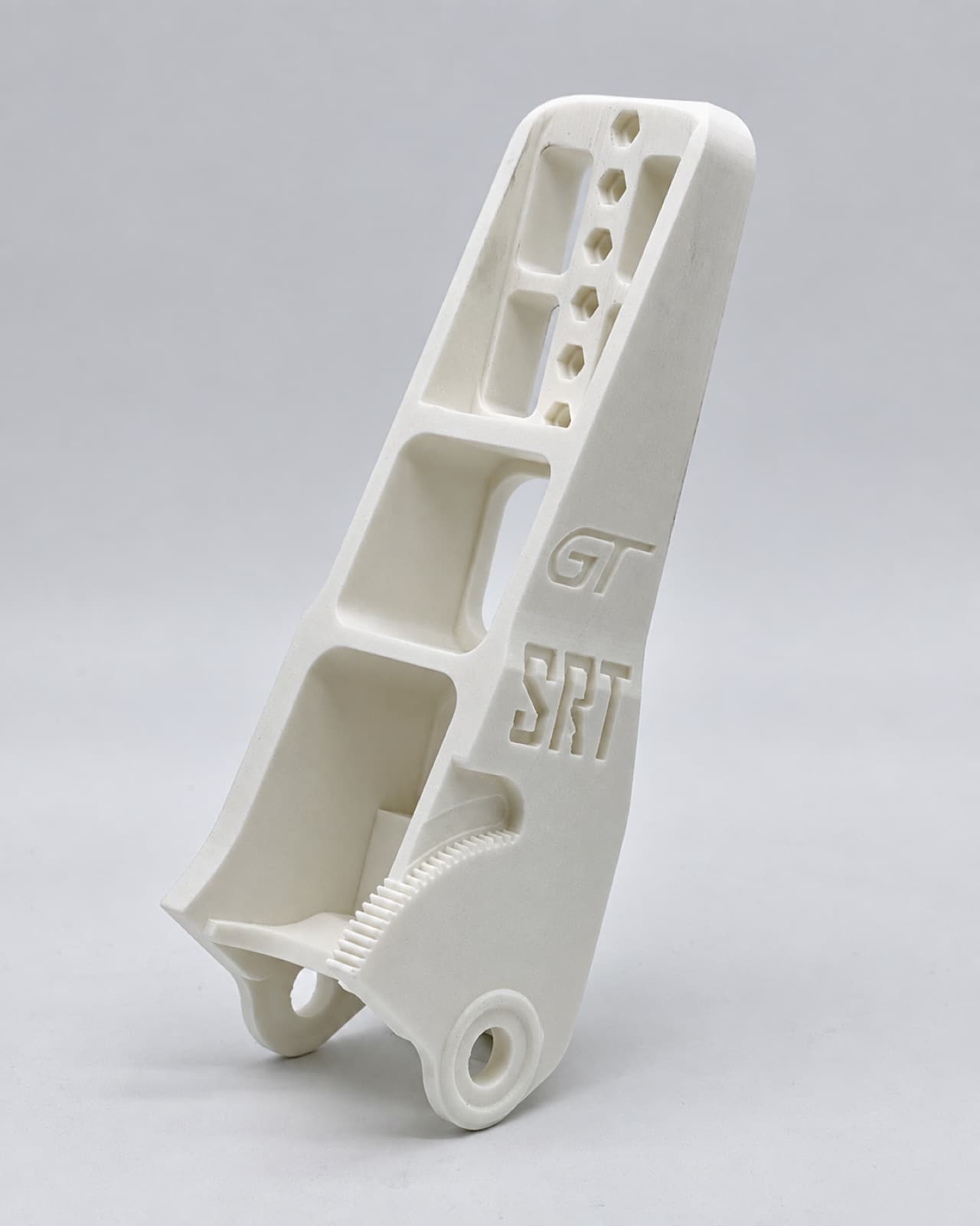 White 3D printed structural bracket with embossed lettering, ribbed pockets and threaded bosses on a white studio sweep
